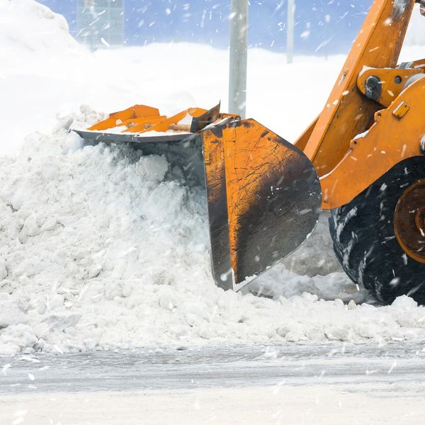 Snowplow clearing snow with an orange loader bucket.