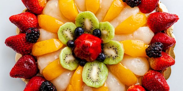 Colorful fruit tart with strawberries, kiwi, peaches, and berries arranged beautifully.