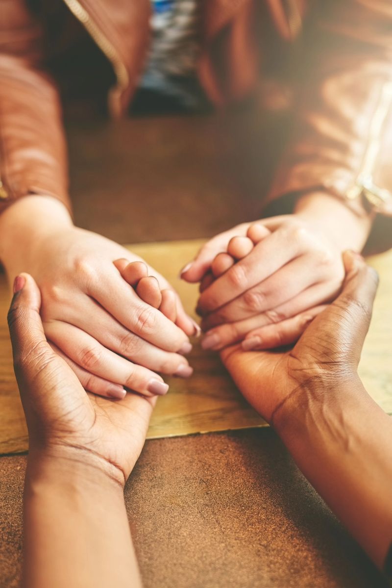 High angle shot of two female friends holding hands in comfort while sitting in their local coffee shop