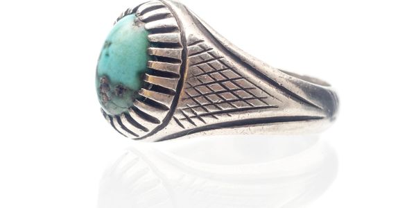 Silver ring with a turquoise stone and intricate side engravings.