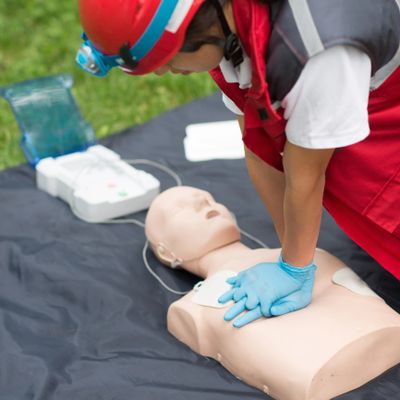 Person practicing CPR on a mannequin with defibrillator nearby.