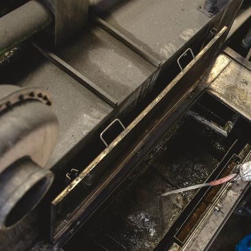 Worker cleaning an industrial machine with a high-pressure hose.