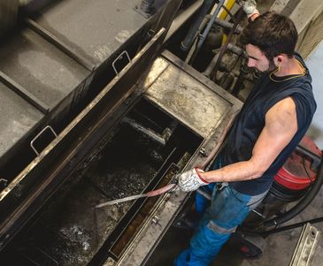 Worker cleaning an industrial machine with a high-pressure hose.