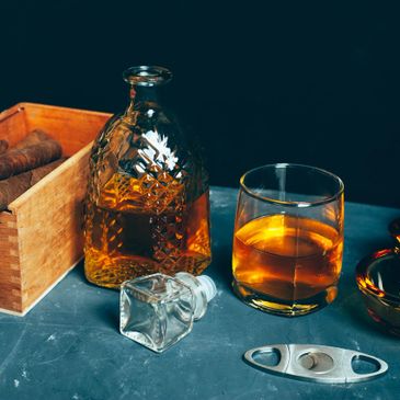 Whiskey glass and decanter with cigars on a table.