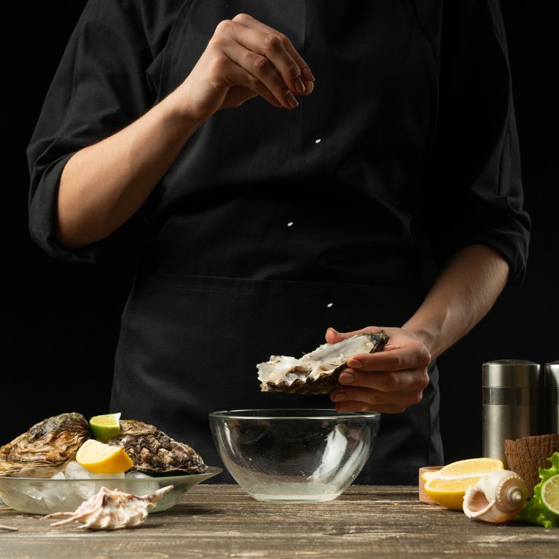 Chef salting oyster with lemon on the background of dry wine on a dark background, menu, restaurant, Italian cuisine, Restaurant business