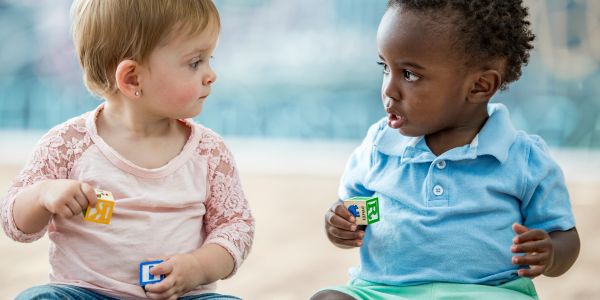 Two toddlers sitting and holding colorful alphabet blocks, looking at each other.