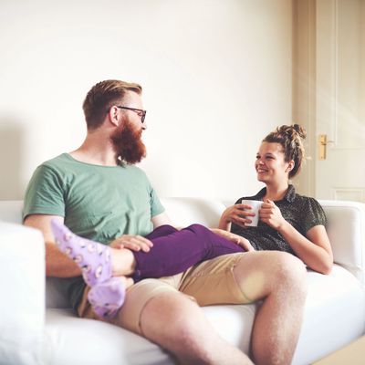 Couple relaxing on a couch, smiling and chatting over coffee.