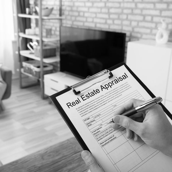 Person filling out a real estate appraisal form on a clipboard in a living room.