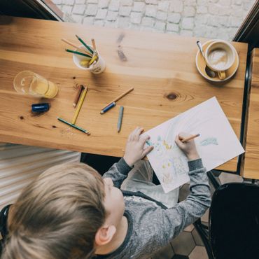 Child drawing with colored pencils at a wooden table.