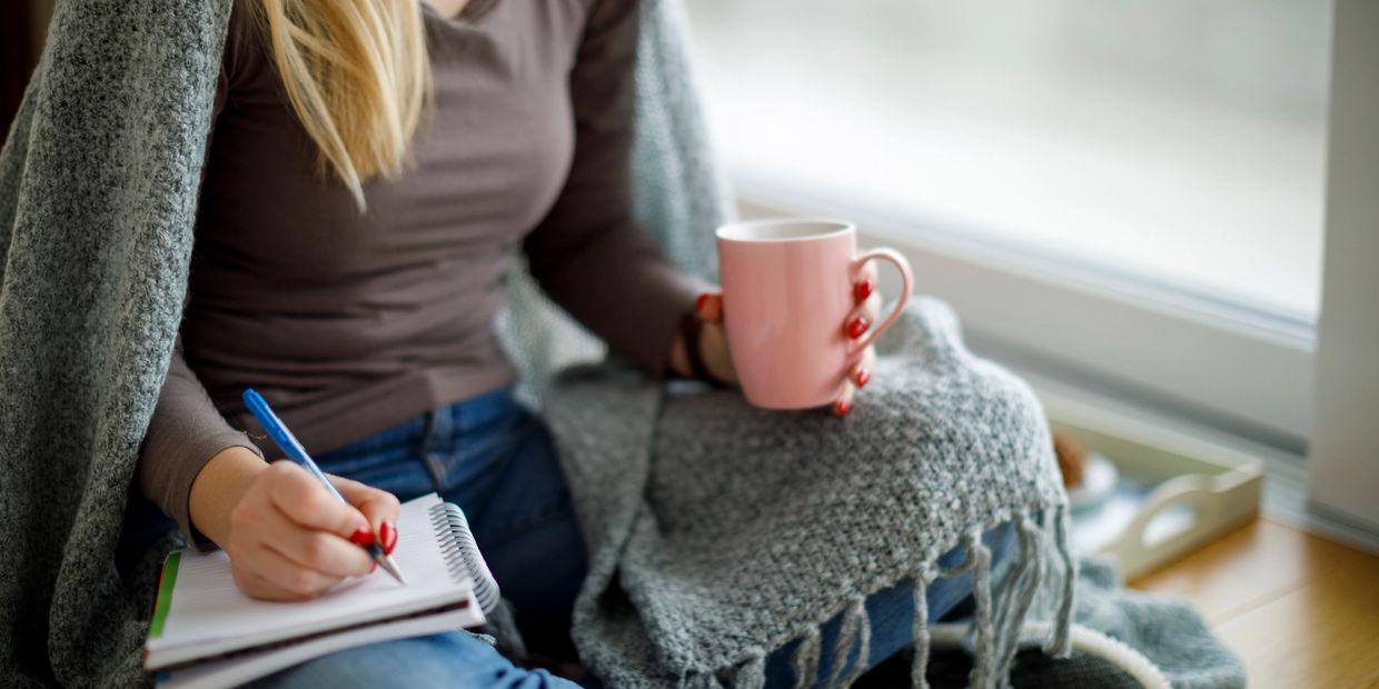 Young woman by a window with tea, journaling for the Healthy Habits Coaching Program.
