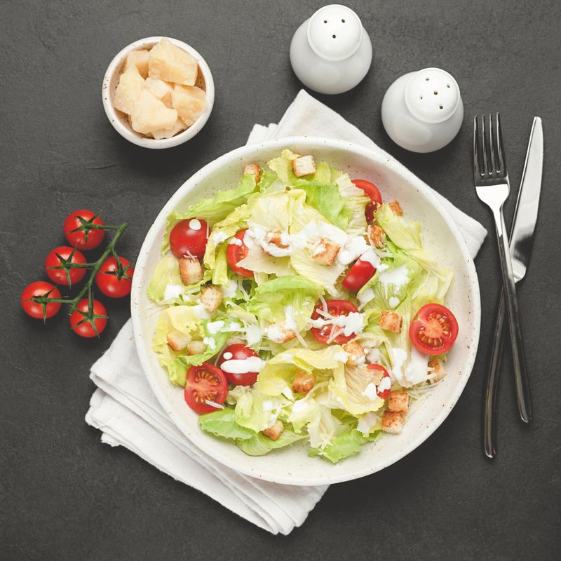 Caesar salad on white plate over black concrete background. Top view, square crop