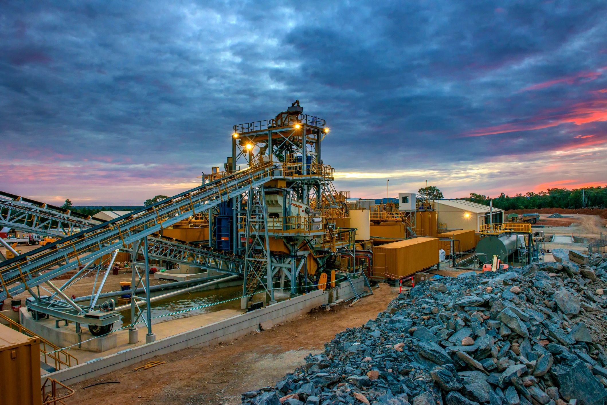 Industrial mining site with machinery under a dramatic sunset sky.