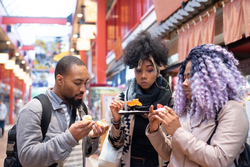 Three millennial travelers trying street foods and snacks while travelling in Japan