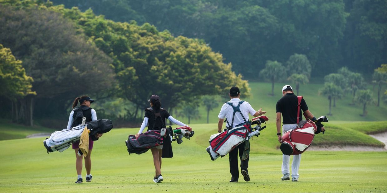 Four people walking on a golf course with golf bags.