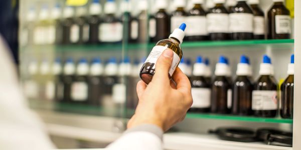 Person holding a medicine bottle in front of pharmacy shelves.