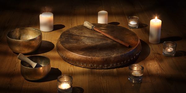 Lit candles surrounding a drum and singing bowls on wood floor.