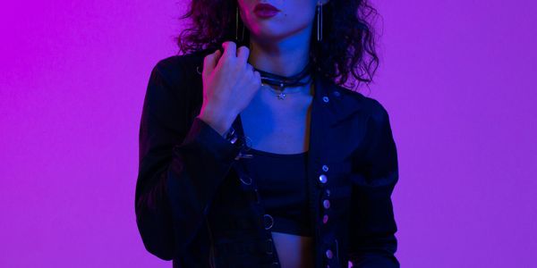 Woman with curly hair in dark clothing under purple-blue lighting.