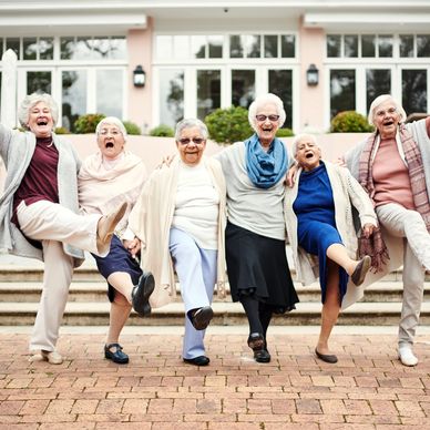 Six elderly residents linking arms & kicking their right legs out in front of them They’re laughing