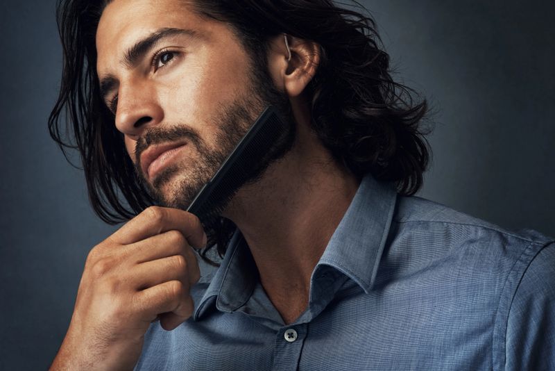 Studio shot of a handsome young man combing his beard against a grey background