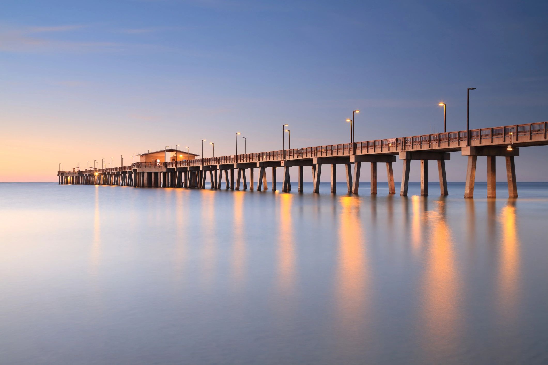 Pier extending into calm water at sunset with lights on.