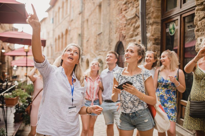 Medium group of people standing in a street in Volterra. They're listening to a tour guide who is talking about the architecture and the history.