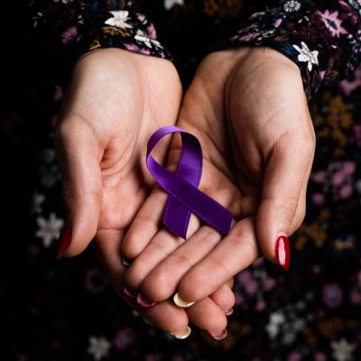 Hands holding a purple awareness ribbon.