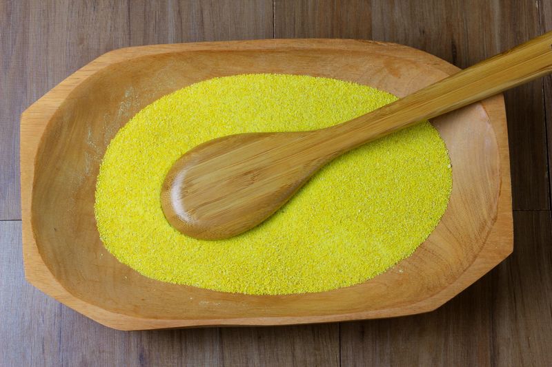 portion of yellow, raw cassava flour, wooden bowl, wooden table, crumbs, top view