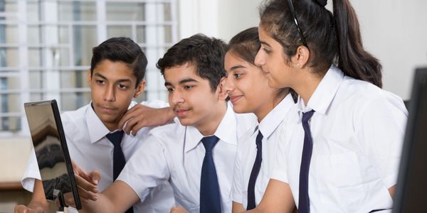 Four students in school uniforms collaborating on a computer project.