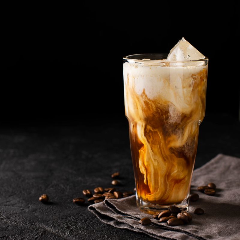 tall glass cold brew coffee with ice and milk on black or dark background