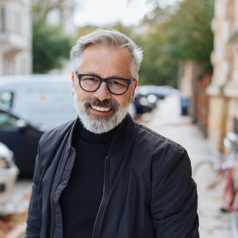 Attractive bearded man with a lovely friendly smile standing in an urban street in a close up portrait