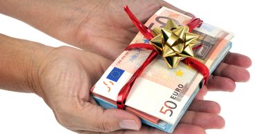 Hands holding a stack of euro banknotes wrapped with a red ribbon and golden bow.