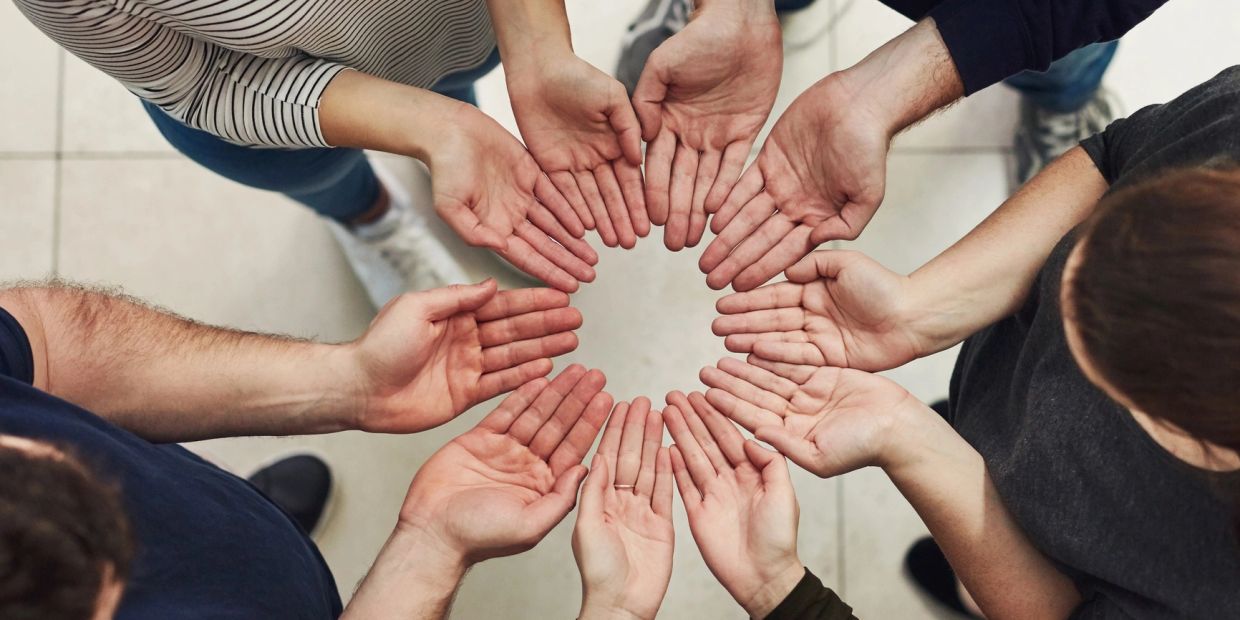 People standing in a circle with hands extended inward.