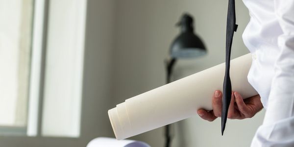 Person holding rolled architectural or engineering blueprints in a bright room.