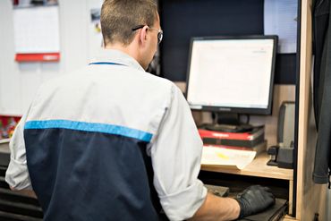 A man in workwear and gloves using a computer at a workstation.