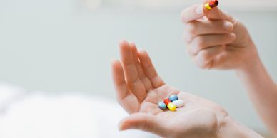 Hand holding various colorful pills with another hand picking one.