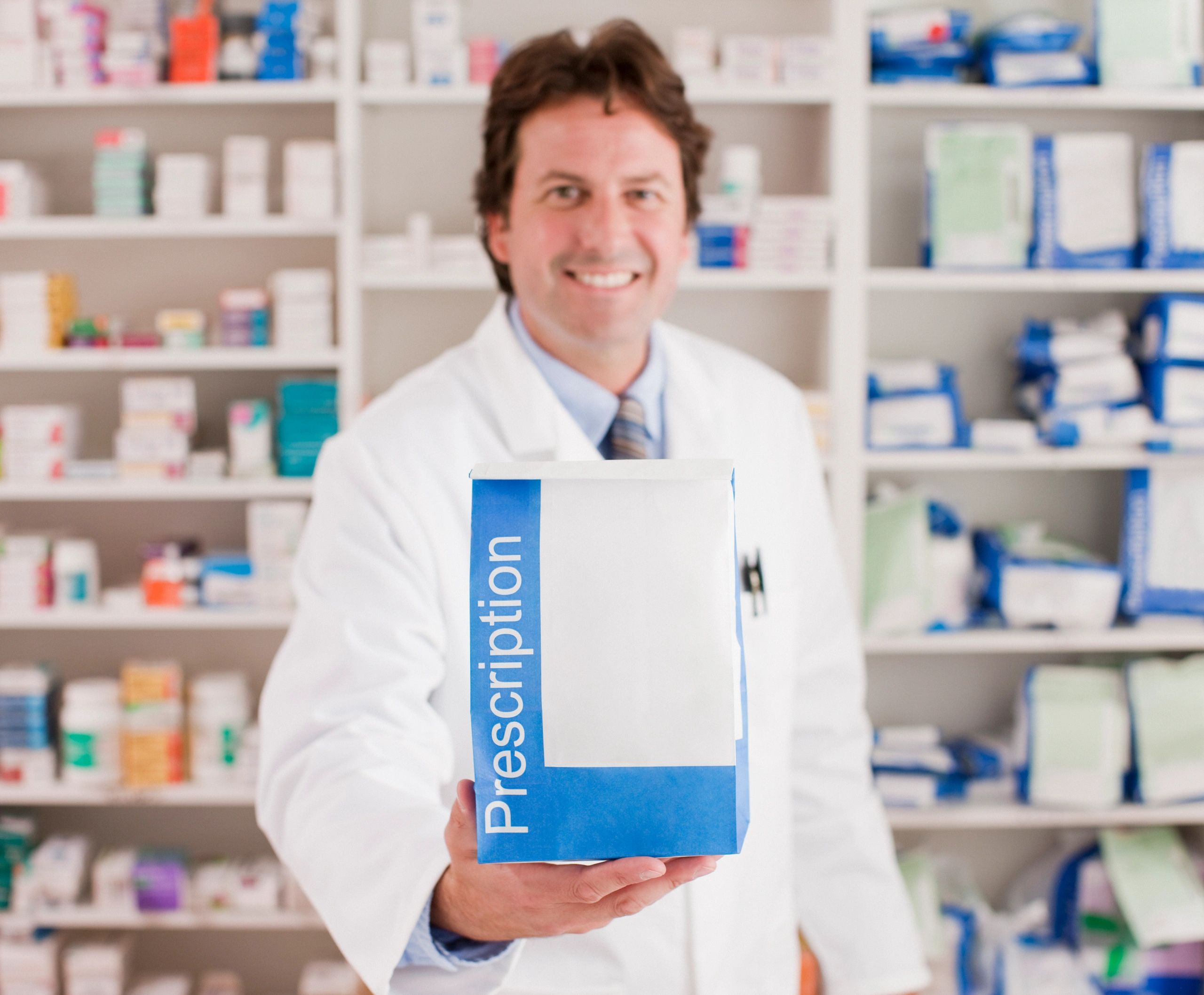 Pharmacist holding prescription bag with medicines in background.