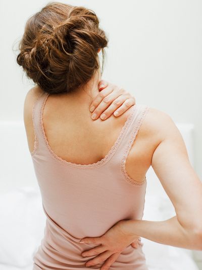 Woman in pink tank top touching her neck and lower back.