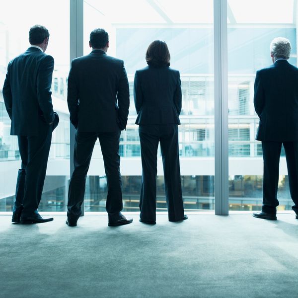 Four business professionals in suits looking out a large window in a modern office.