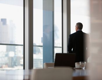 Man in suit looking out office window.