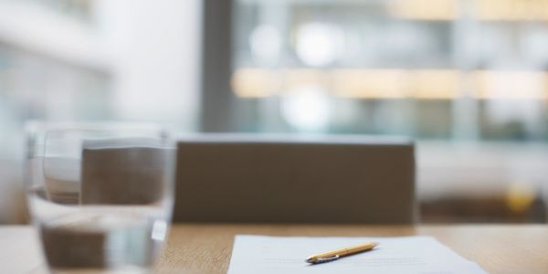 Pen resting on a document on a wooden table with a glass of water nearby.