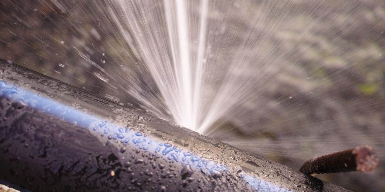 Water spurting from a damaged black pipe with a blue stripe.