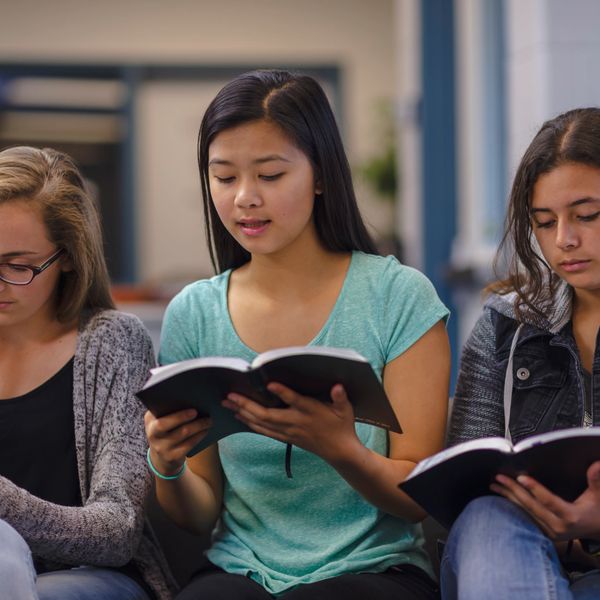 Three young women reading books together indoors.