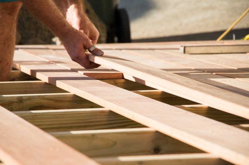 Man placing a plank of wood in a deck home renovation on a warm sunny day