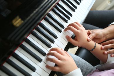 Adult guiding a child's hands while playing piano keys.