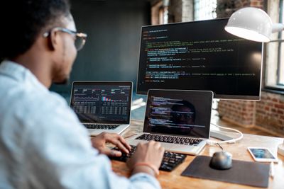 A programmer working with multiple screens displaying code and data charts.