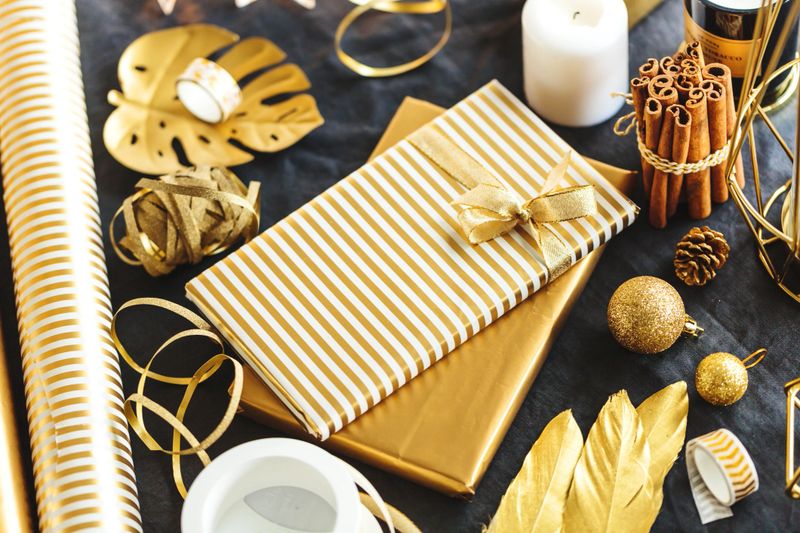 Beautiful wrapped in golden paper gifts with golden christmas deco on table. Closeup.