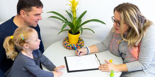 Adult woman explaining paperwork to a man and a child at a table.