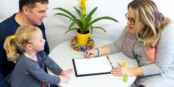 A woman discusses paperwork with a man and child at a round table.