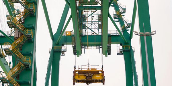 Large green industrial crane lifting a yellow container spreader.