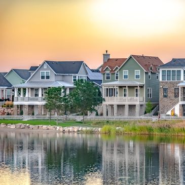 Lakeside houses reflecting on calm water at sunset.